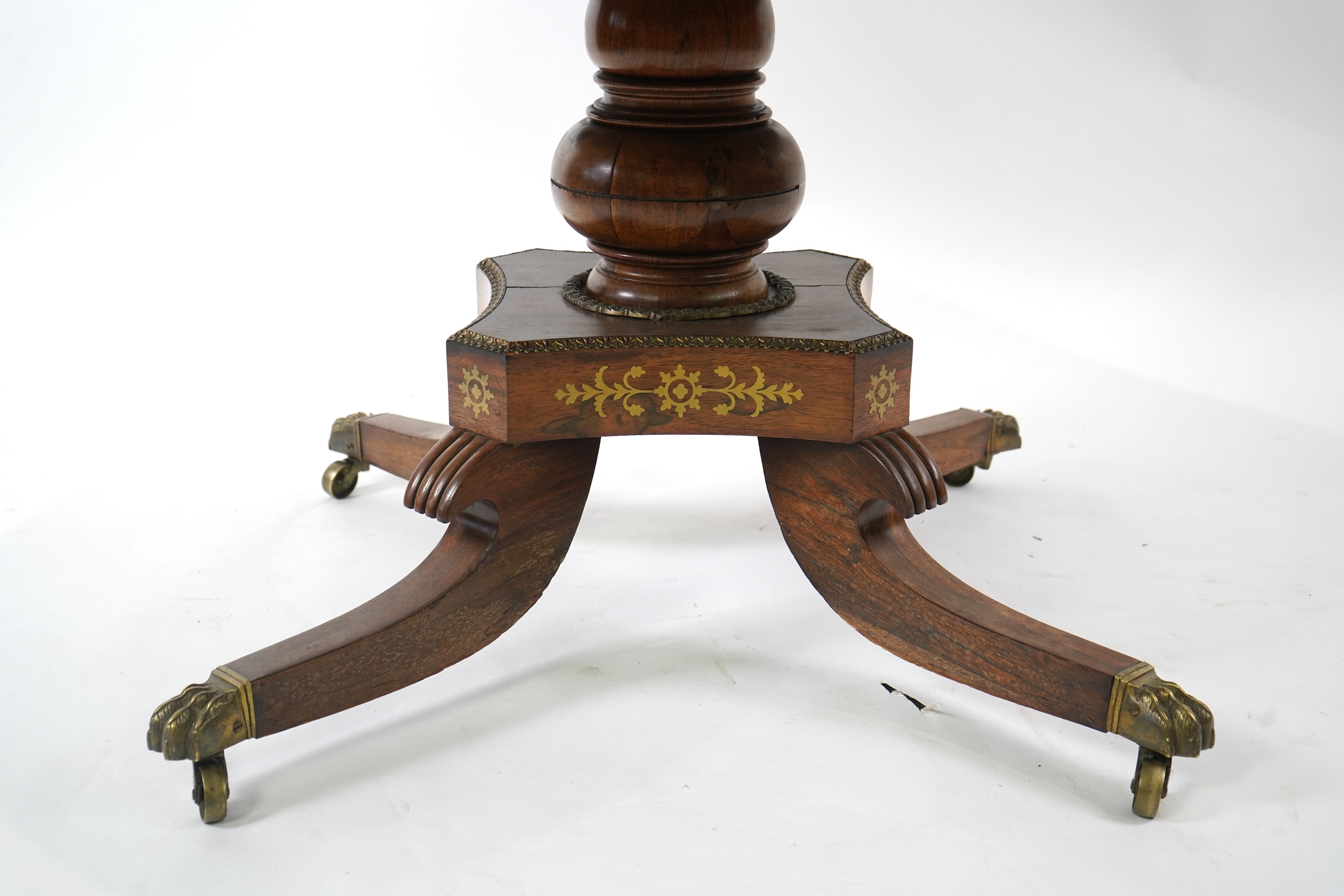 A Regency cut brass inlaid and gilt metal mounted circular rosewood breakfast table, the bird's-eye maple banded tilt top on baluster column, concave platform and quadruple downswept base with cast claw caps and castors,